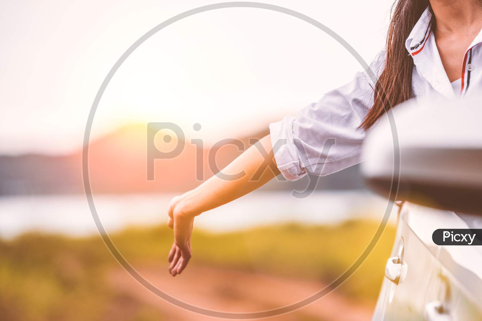 Happy Woman Waving Hand Outside Open Window Car With Meadow And Mountain Lake Background. People Lifestyle Relaxing As Traveler On Road Trip In Holiday Vacation. Transportation And Travel Concept