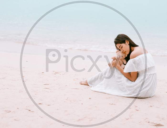 Asian Woman Hug Bear Doll And Waiting For Love That Make Her Happy At Beach. Lonely And Beauty Concept. Back View Scene Of Girl. Ocean And Sea Theme. Copy Space In Left Side. Soulmate Theme.