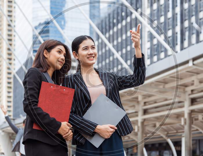 Two Young Businesswomen Looking And Pointing Forward For Thinking Of Future Plan And Sale Break Even Point After Marketing. Business Teamwork Employees Of Lifestyle Working Women. Boss And Secretary