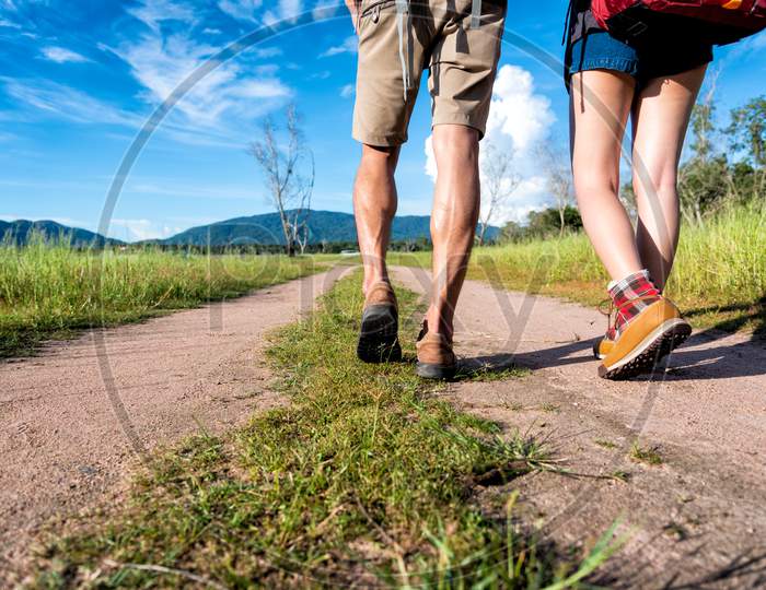 Close Up Of Lower Legs Of Two Travelers Walking Along Path In Nature. Hiking And Camping Concept. Backpacker An Tourist Concept. Outdoors Activity And Adventure Theme.