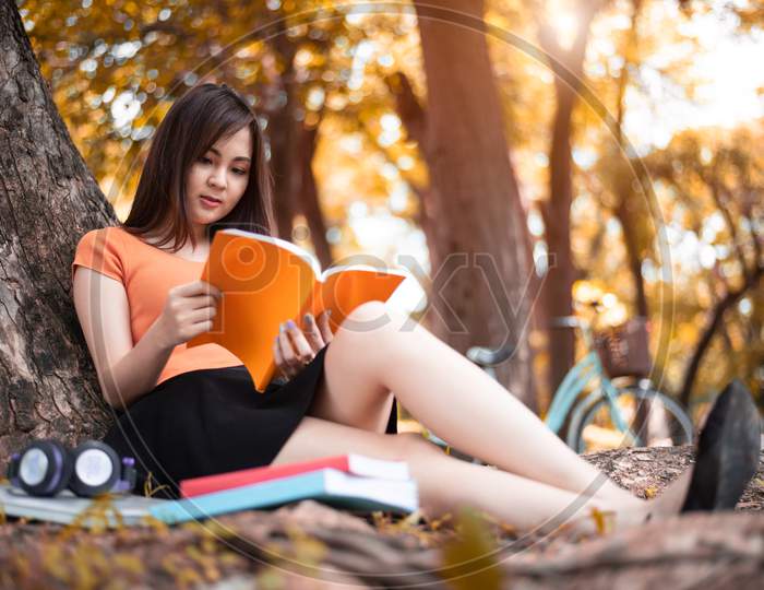 Asian Beauty Woman Reading Book In Park. People Lifestyles And Entertainment Concept. Relaxation And Vacation Concept. Autumn And Fall Seasonal Theme.