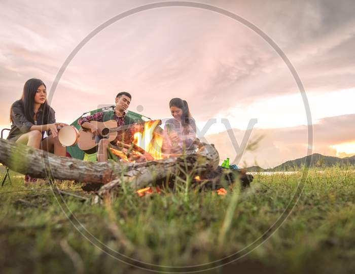 Group Of Travelers Camping And Doing Picnic And Playing Music Together. Mountain And Lake Background. People And Lifestyle. Outdoors Activity And Leisure Theme. Backpacker And Hiker. Dawn And Twilight