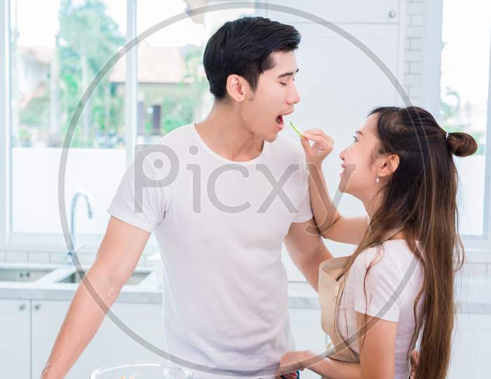 Woman Feeding Cucumber To Man As Lovers Or Couples In Kitchen Room. Cooking And Honeymoon And Wedding Concept