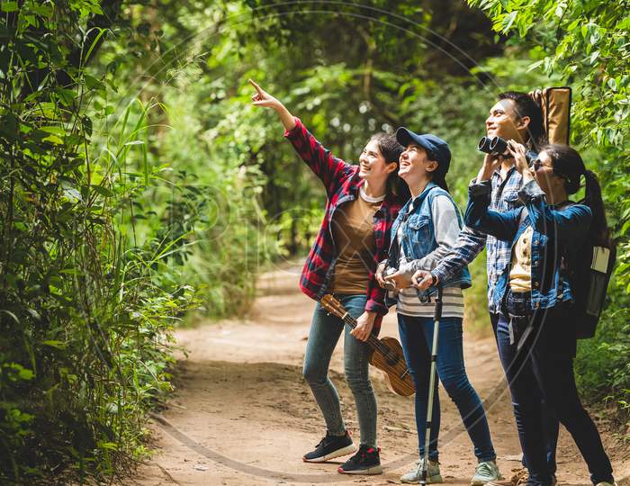 Group Of Asian Friends Team Adventure For Hiking And Camping In Forest Together. Family Travel Relaxation. Trekking And Trail Activity In Wild Life Concept. Woman Pointing At Tree Or Sky. Copy Space