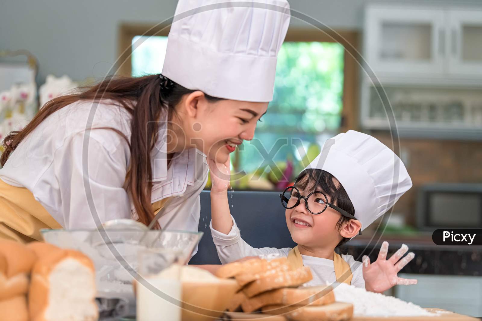 Cute Little Asian Boy Painting Beautiful Woman Face With Dough Flour. Chef Team Playing And Baking Bakery In Kitchen Funny. Homemade Food And Bread. Education And People Lifestyles Learning Concept