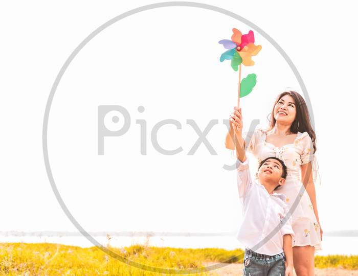 Little Asian Boy And His Mom Playing Colorful Rainbow Turbine In Meadow. Mother And Son Playing Together. Celebrating In Mother Day And Appreciating Concept. Summer People And Lifestyle Theme.