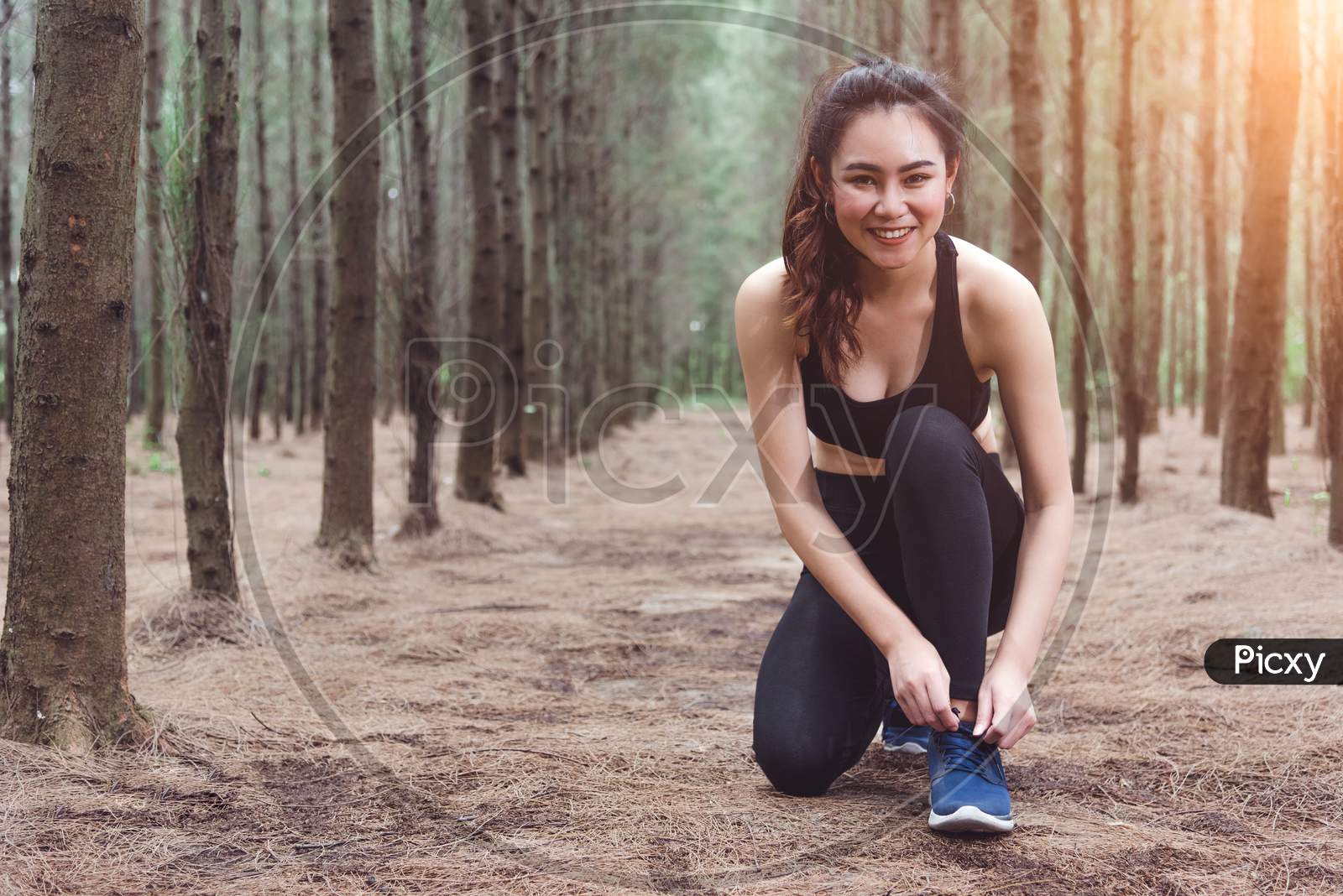 Woman Tying Up Shoelaces When Jogging In Forest Back With Drinking Water Bottle Beside Hers. Sneakers Rope Tying. People And Lifestyles Concept. Healthcare And Wellness Theme. Park And Outdoors Theme.