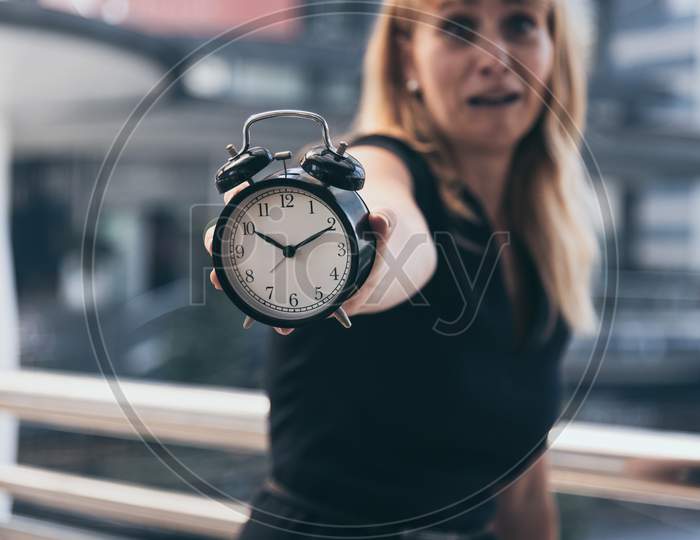 Business Women Show Alarm Clock And Shocked With Late In Rush Hours When Going To Work In City Urban Background. Deadline And Wake Up Late. People Lifestyle And Daily Life Planner Concept.