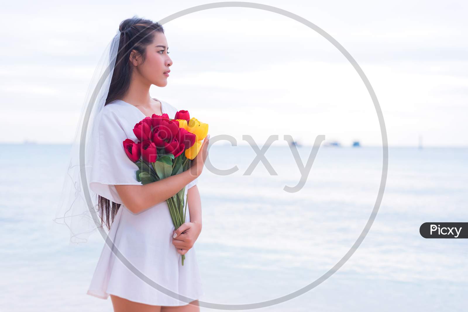 Asian Woman Holding Flowers And Waiting For Someone Make Her Happy. Lonely And Single Woman Concept. Sadness And Destiny Concept. Beauty And Nature Theme. Ocean And Sea Theme. Finding Soulmate Theme.