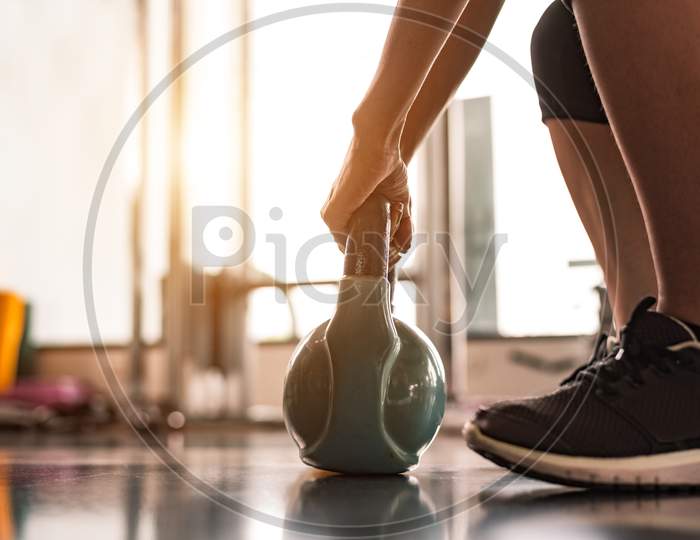Close Up Of Woman Lifting Kettlebell Like Dumbbells In Fitness Sport Club Gym Training Center With Sport Equipment Near Window Background. Lifestyles And Workout Exercise For Bodybuilding And Healthy