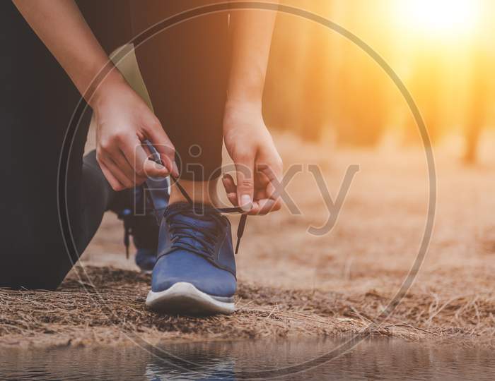 Young Fitness Running Woman Tying Shoelaces At Outdoors In Forest Background. Sport And Nature Concept. Countryside Exercise And And Athlete Activity Concept. Healthy And Lifestyle Theme.