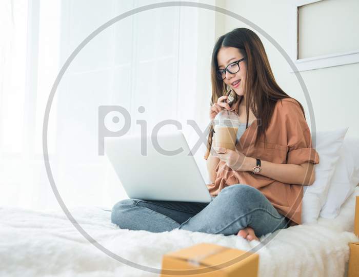 Beauty Asian Woman Using Laptop And Drinking Coffee On Bed. Business And Technology Concept. Delivery And Online Shopping Concept. Post And Service Theme.
