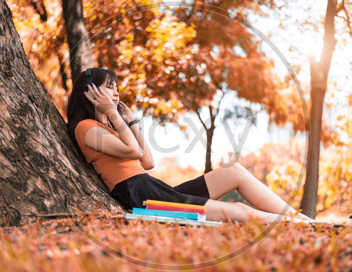 Asian Beauty Woman Listen To The Music In Park. People Lifestyles And Entertainment Concept. Relaxation And Vacation Concept. Autumn And Fall Seasonal Theme.