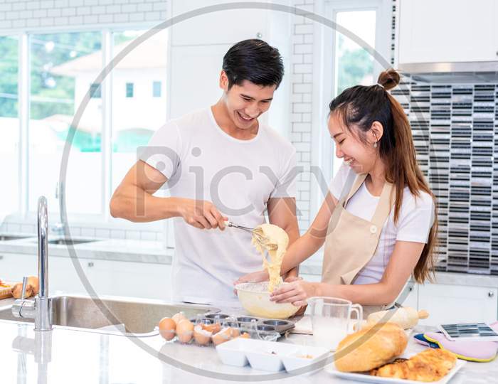 Happy Asian Couples Cooking And Baking Cake Together In Kitchen Room. Man And Woman Looking To Tablet Follow Recipe Step At Home. Love And Happiness Concept. Sweet Honeymoon And Valentine Day Theme