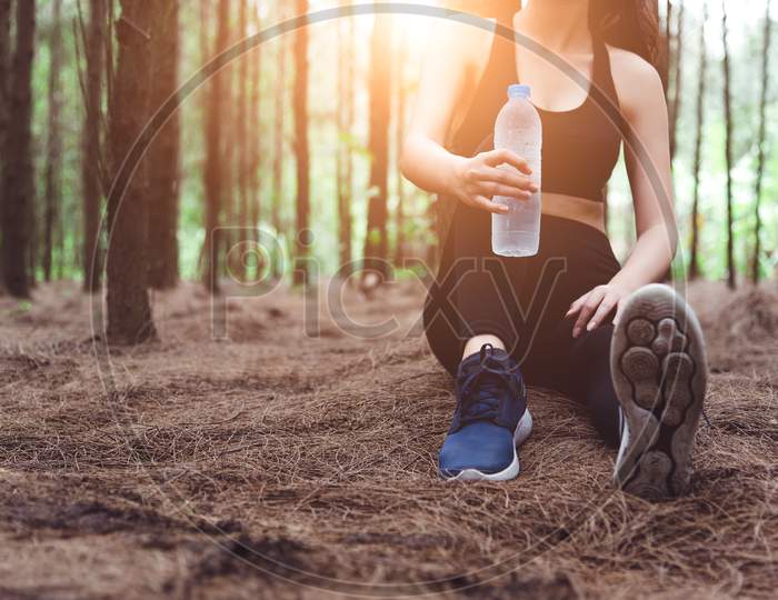Close Up Of Beauty Sport Woman Resting And Holding Drinking Water Bottle And Relaxing In Middle Of Forest After Tired From Jogging. Girl Sitting And Looking Attraction View. Workout Lifestyle Concept