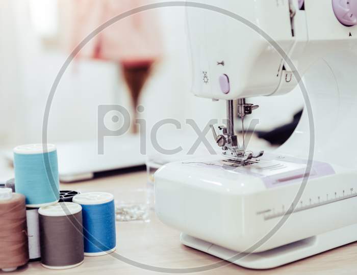 Closeup Of Sewing Machine With Fashion Designer Showroom Studio Workshop Background With New Collection Of Pink Pastel Female Clothes Design. Tailor And Sewing Concept. Dressmaker Modern Room Interior