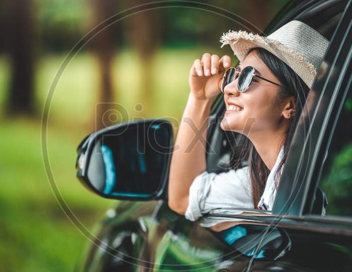 Happy Woman Hand Holding Hat Outside Open Window Car With Green Forest Woods Mountain Background. People Lifestyle Relaxing As Traveler On Road Trip In Holiday Vacation. Transportation And Travel