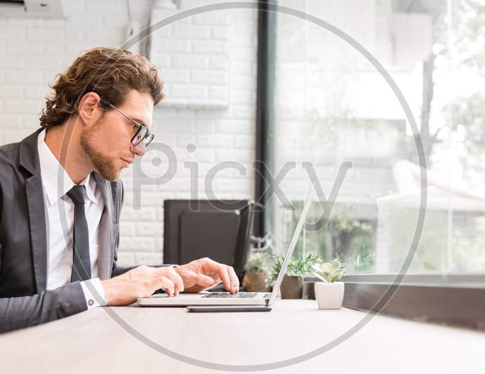 Business Man Working Hard With Laptop On Desk In Office Near Window. Business And Success Concept. People And Occupation Concept. Technology And Computer Theme. Indoors And Interior Theme