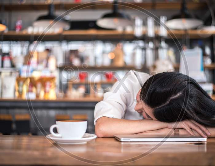 Asian Woman Is Resting And Sleeping In A Coffee Shop Because She Is Tired Of Working All Night. Business Owner And Freelance Concept. Healthcare And Relaxation Theme.