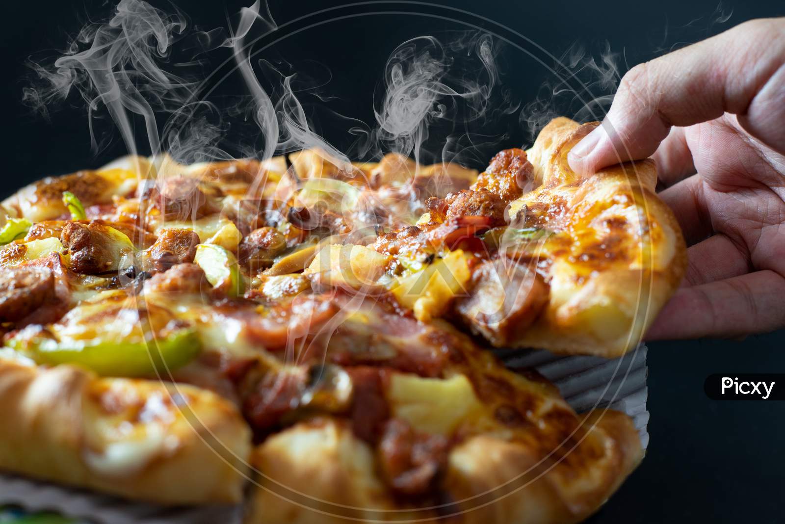 Hand Picking Sliced Pizza With Cheese Ham Bacon And Pepperoni On Black Background With Hot Steaming Smoke. Food And Cooking Concept. Lunch Time Serve And Hungry Theme. Pizza Delivery Service To Home.
