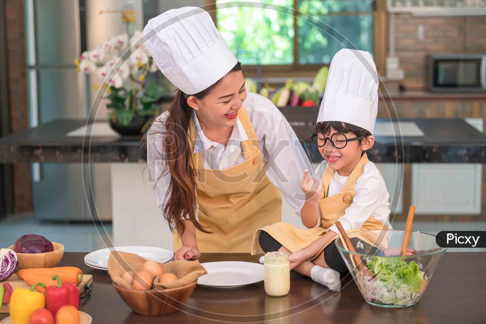 Happy Beautiful Asian Woman And Cute Little Boy With Eyeglasses Prepare To Cooking In Kitchen At Home. People And Family Concept. Homemade Food And Ingredients Concept. Two Thai People Lifestyles