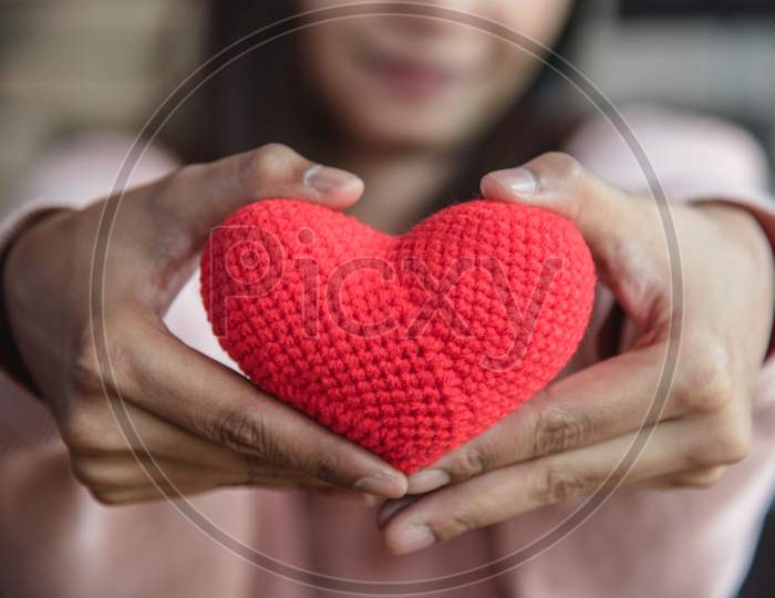 Big Red Yarn Heart Holding And Giving To Front By Woman Hand. Love And Affection In Valentines Day Concept. Romantic Object And Health Care.