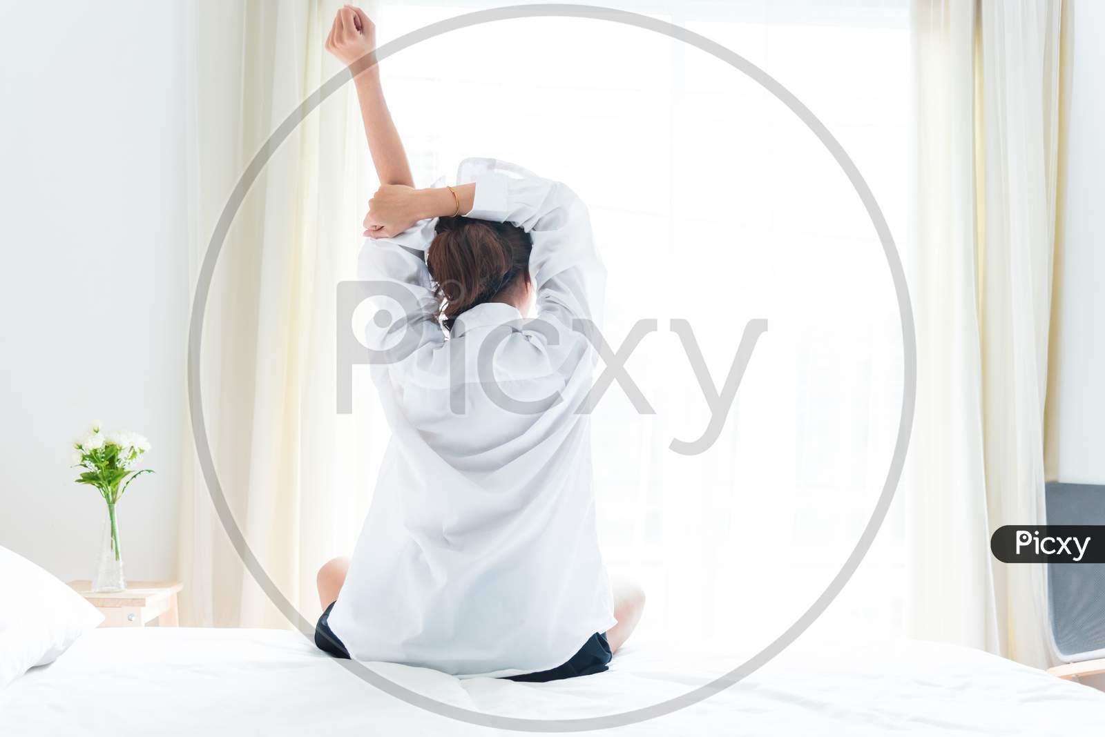 Back View Of Woman Stretching In Morning After Waking Up On Bed Near Window. Holiday And Relax Concept. Lazy Day And Working Day Concept. Office Woman And Worker In Daily Life Theme
