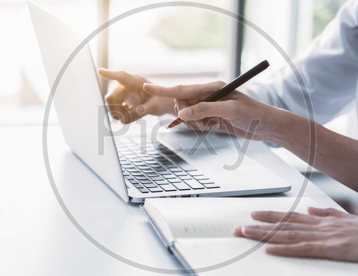 Close Up Of Two Businesswoman Using Laptop And Writing On Notebook In The Morning. Business And Financial Concept. People And Lifestyles Concept. Office And Workplace Theme.
