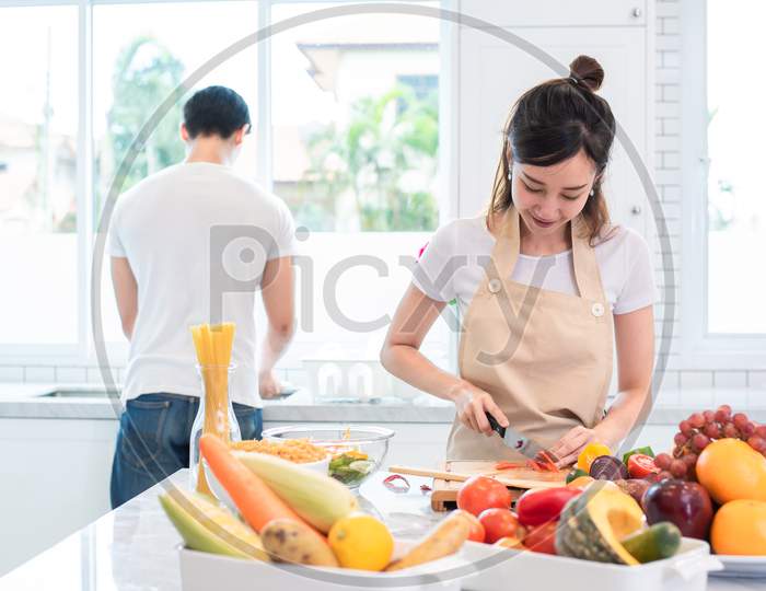 Asian Lovers Or Couple Cooking And Slicing Vegetable In Kitchen Room. Holiday And Honeymoon Concept. Valentine Day And Wedding Theme