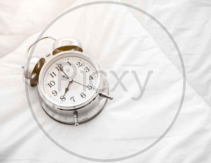 Ringing Alarm Clock On White Bed Sheet. Top View Of Object. 8 O Clock Setting Up