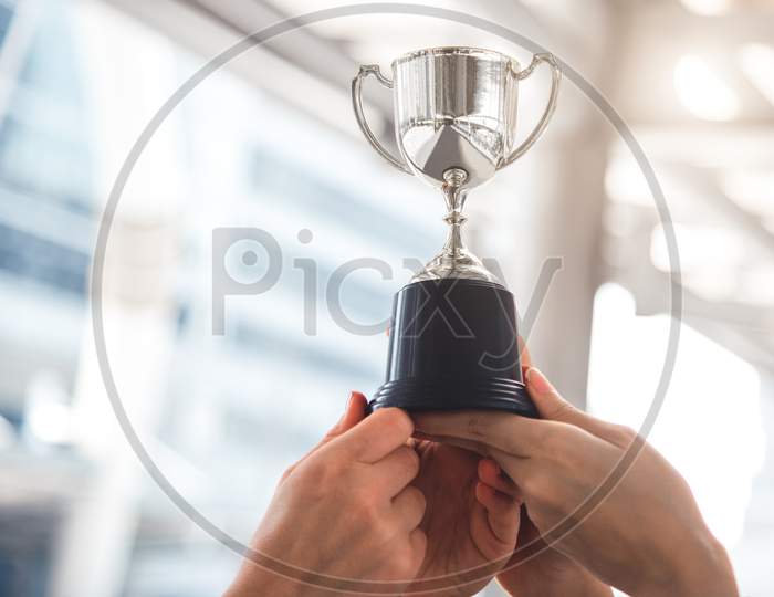 Champion Silver Trophy For Runner Up Winner With Sport Player Hands In Sport Stadium Background. Success And Achievement Concept. Cup Award Theme. American Football Award And Match Game Play Prize