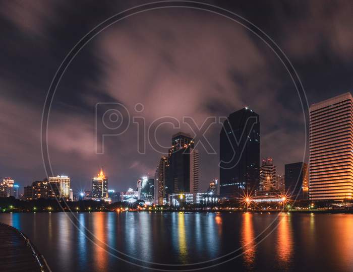Big City In The Night Life With Reflection Of Water Wave. Long Exposure Technics. Panorama Of Landscape.Town And Urban Concept. Landscape And Attraction Theme.