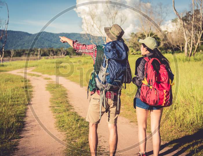 Two People Walking On Path In Meadow Field. Male And Female Traveler Looking At Attraction View Point. Couples Adventure At Outdoors Together. People And Lifestyles Concept. Trip And Camping Theme.