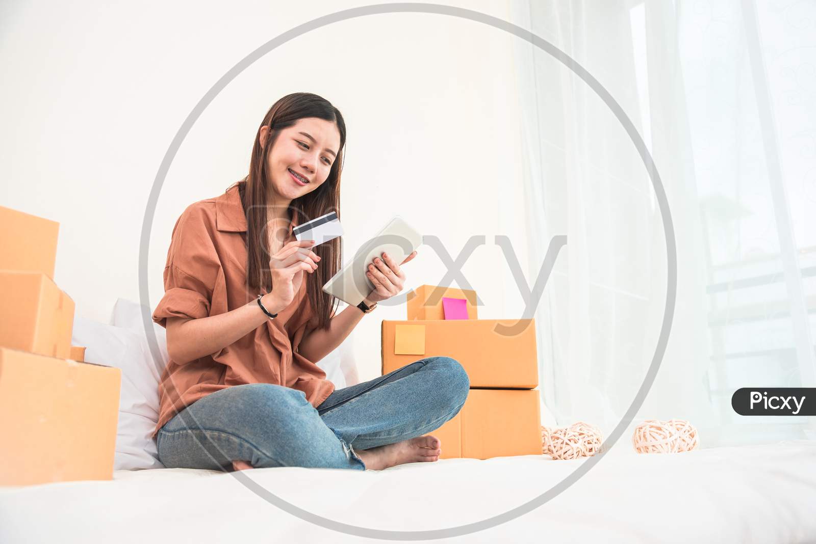 Young Asian Woman Startup Small Business Entrepreneur Sme Distribution Warehouse With Parcel Mail Box. Owner Home Office. Online Marketing And Product Packaging And Delivery Service. Credit Card Use