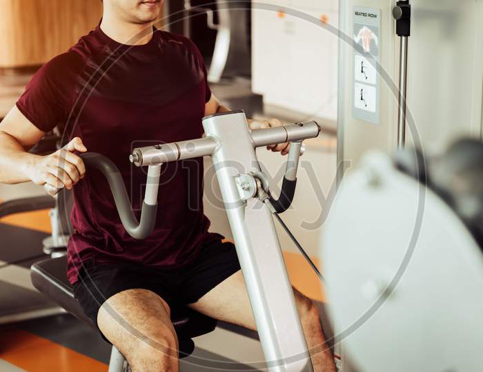 Front View Of Sport Man Using Back Muscle Stretch Machine Called Seated Row In Fitness Gym. People Lifestyles And Sport Workouts Concept. Close Up View