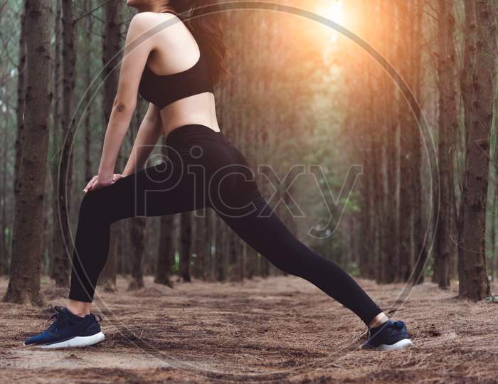 Close Up Of Lower Body Of Woman Doing Yoga And Stretching Legs Before Running In Forest At Outdoors. Sports And Nature Concept. Lifestyle And Activity Concept. Pine Woods Theme.