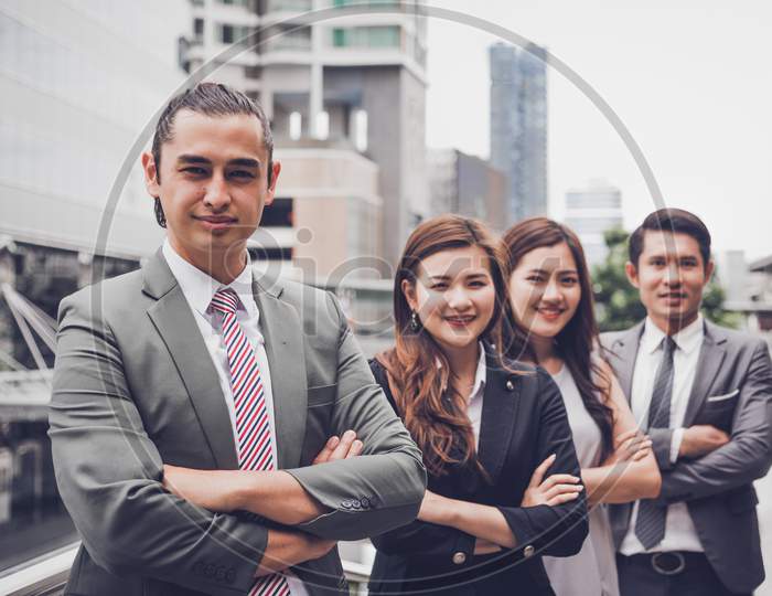 Business People Team Doing Confident Gesture Portrait At Outdoor In City. Multiculturalism Of Asian And Caucasian Occupation. Happy Teamwork Business Professional Leadership In Suit. Looking Camera