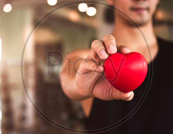 Happy Sport Man Holding Red Heart In Fitness Gym Club. Medical Cardio Heart Strength Training Lifestyle. Handsome Sport Male Workout Exercise. Cardiac Healthy And Well-Being. Massage Ball In Hand