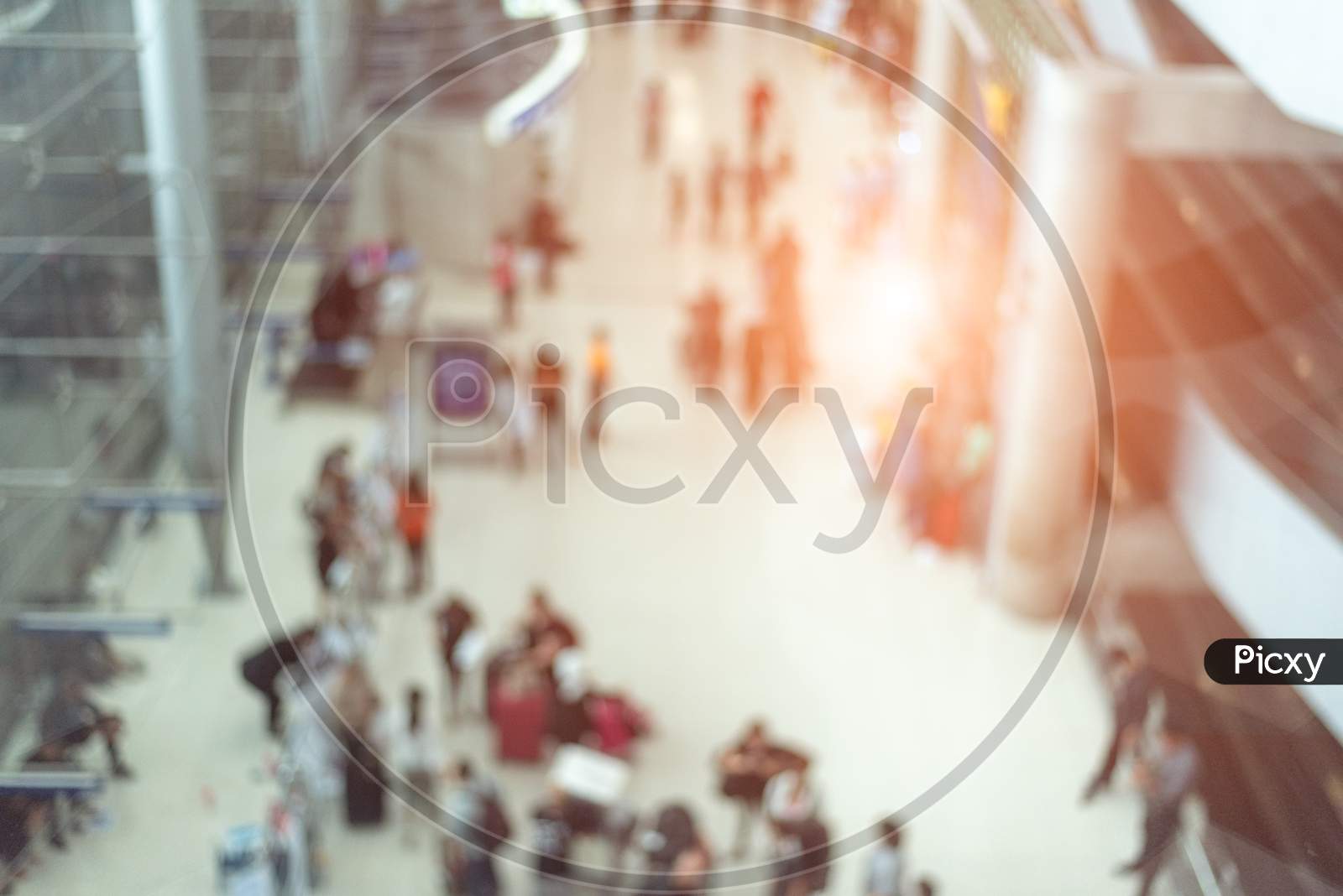 Blurry Background Of Airport Terminal And Convention Hall With Crowd People. Orange Sun Light Element. Business And Travel Concept. Abstract Background Theme.