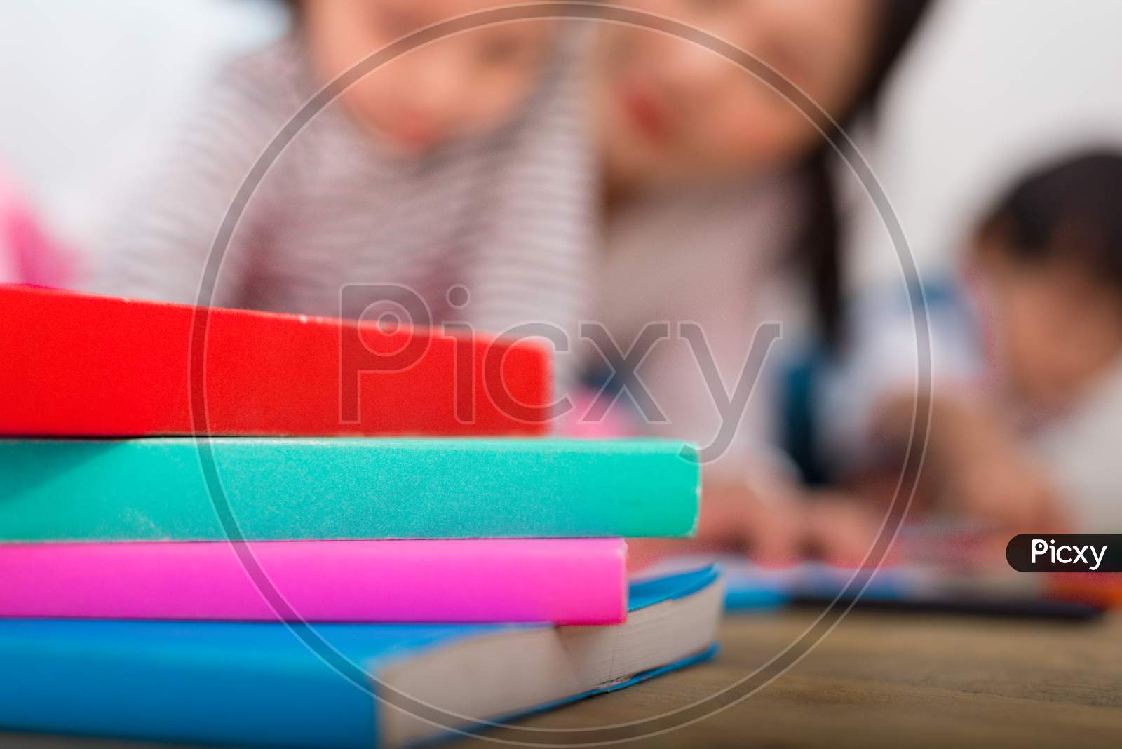 Stack Of Colorful Book On Floor With Blurry Woman And Two Kids Background. Education And Learning Concept. Object Theme