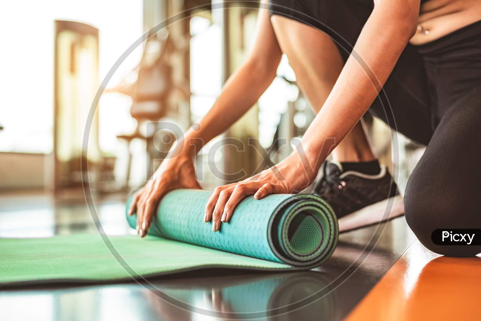 Close Up Of Sporty Woman Folding Yoga Mattress In Sport Fitness Gym Training Center Background. Exercise Mat Rolling Keeping After Yoga Class. Workout And Sport Training Concept. Hands On Carpet