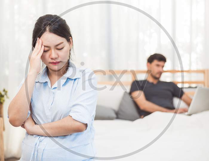 Pregnant Woman Worried About Husband Neglect To Take Care Of Her Health And Baby. Wife With Ignored Workaholic Husband Using Laptop Computer Background. Social Issue Problems Of Family In Home Bedroom