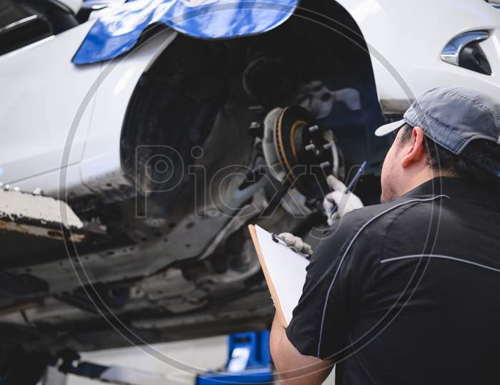 Asian Male Car Technician Car Maintenance For Customers According To Specified Vehicle Maintenance Checklist. Disk Brake Pad Wear Automotive Repairing On Vehicle. Safety Inspection Check Service