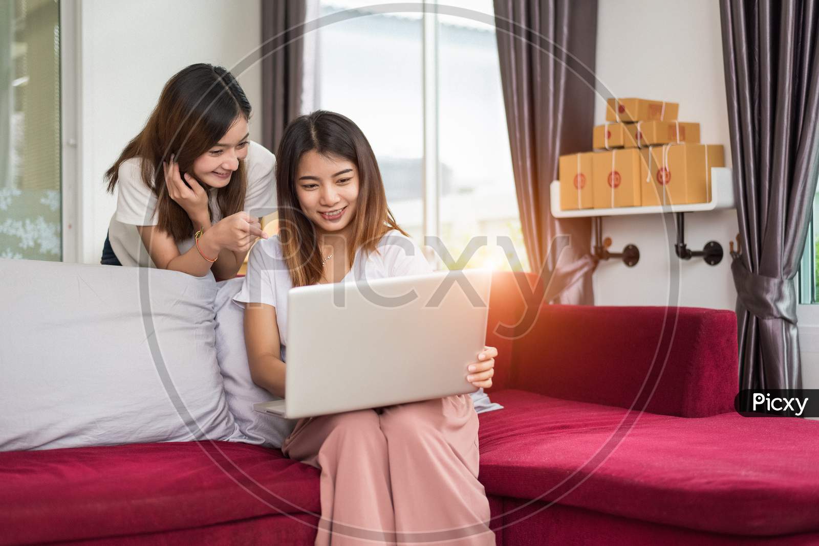 Two Young Freelancer Asian Girl Businesswomen Private Working At Home Office With Laptop Computer Sitting On Sofa. Packaging Delivery Online Shopping Service And Marketing Advertising To Customer