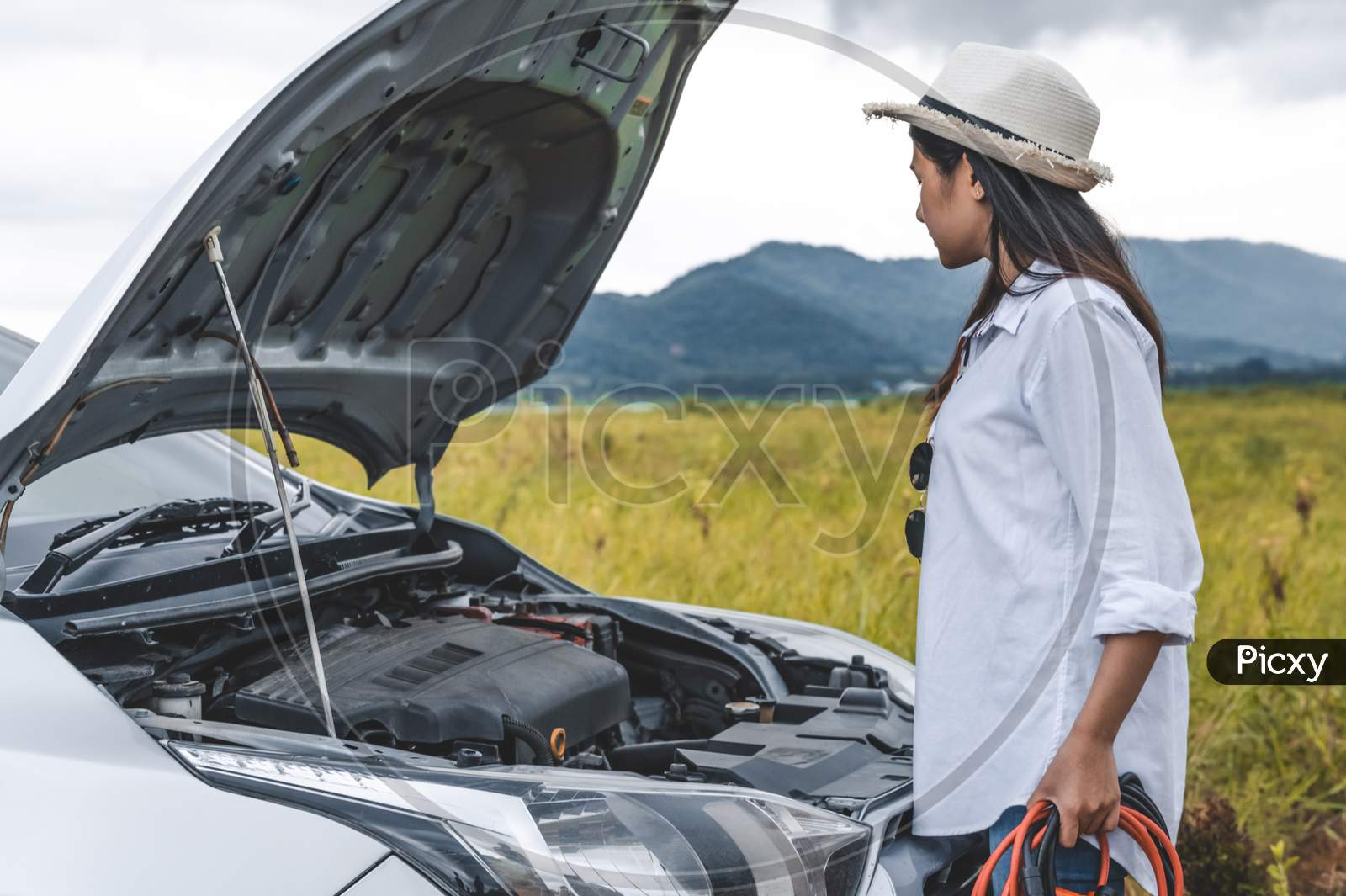Asian Woman Holding Battery Booster Cable Copper Wire For Repairing Breakdown Broken Car By Connect With Red And Black Line To Electric Terminal By Herself. Car Maintenance And Transportation Concept