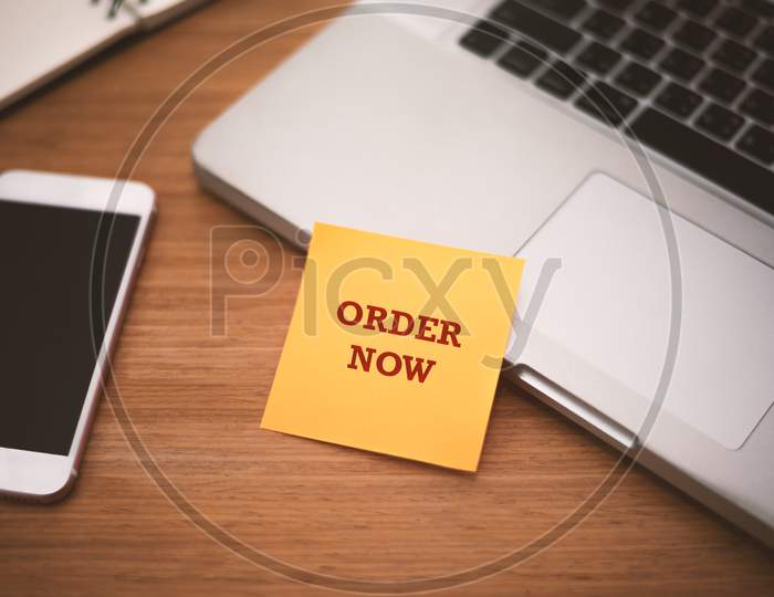"Order Now" Text On Post It Paper Near Laptop And Smart Phone On Wood Table, Online Shopping And Technology Marketing Concept. Split And Cross Processing Tone Pinterest And Instragram Like Process.