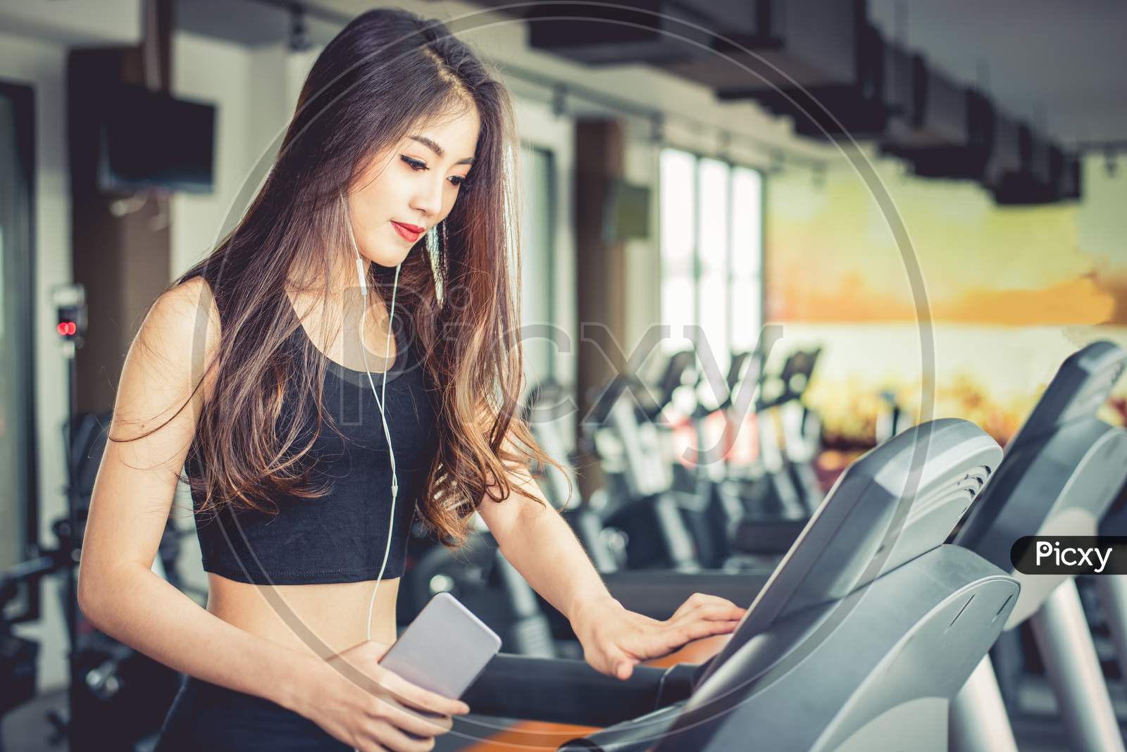 Asian Woman Using Smart Phone When Workout Or Strength Training At Fitness Gym On Treadmill. Relax And Technology Concept. Sports Exercise And Health Care Theme. Happy And Comfortable Mood.