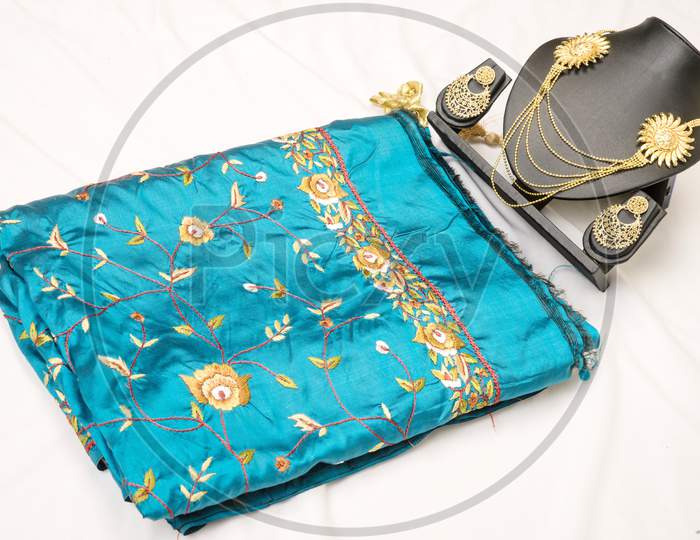 Folded blue colour fabric  placed on a white  background kept with Indian Jewelries