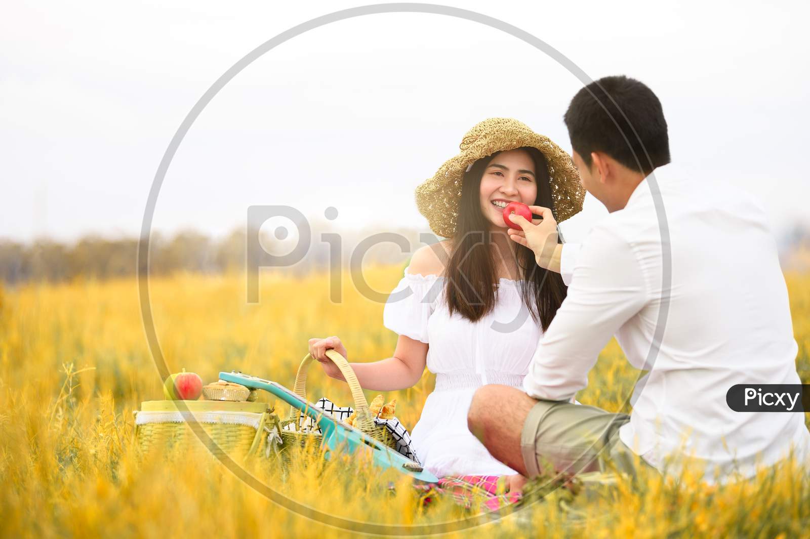 Asian Couple Doing Picnic In Golden Autumn Meadow Grass Field As Honeymoon Trip After Wedding. Valentines Day And Family Love Concept. Outdoors Nature And Long Vacation Relaxation. People Lifestyes