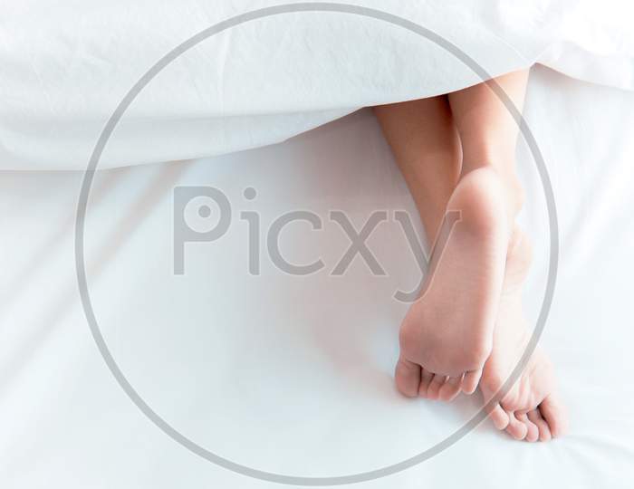 Woman Feet On The Bed Under White Blanket. Sleeping And Relax Concept. Vacation And Holiday Theme